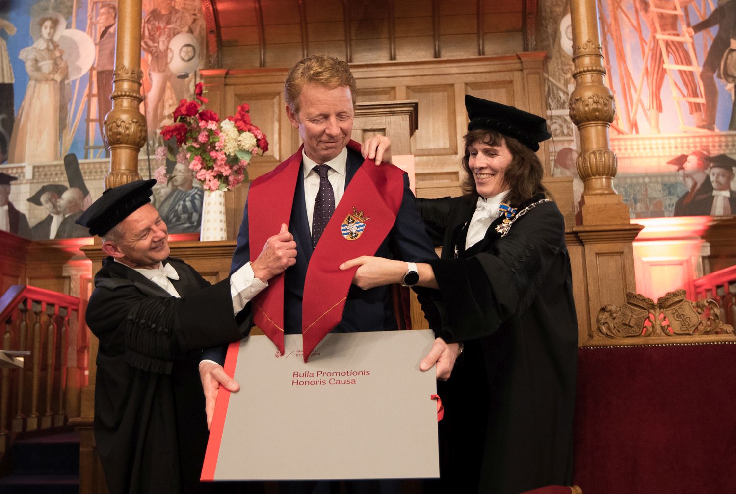 Gerrit Hiemstra krijgt de kappa omgehangen met hulp van decaan van de Faculty of Science and Engineering Joost Frenken en rector magnificus Jacquelien Scherpen. Foto: Gerhard Taatgen